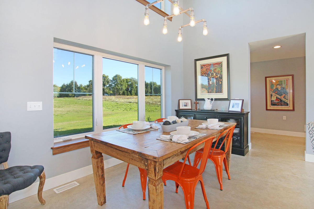 Dining area of a custom-built West Michigan home by R-Value Homes, with large windows and a rustic wooden table