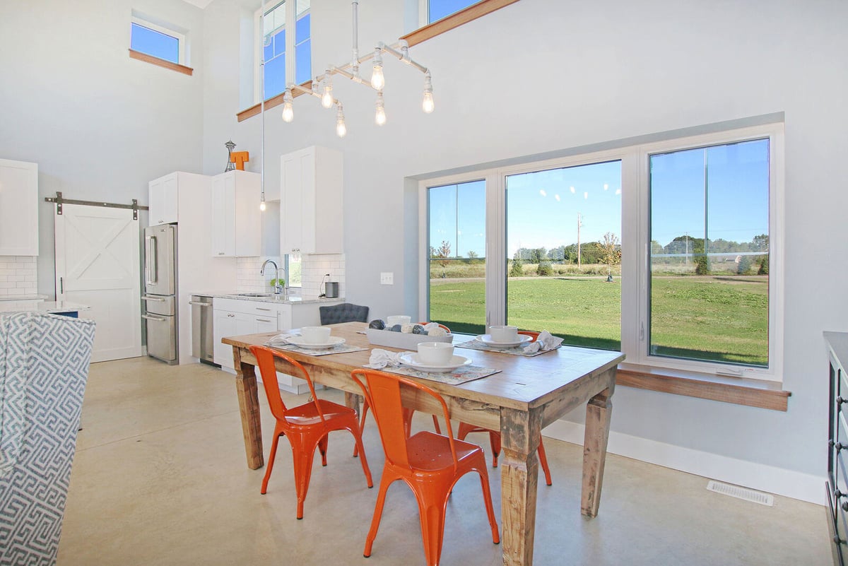 Modern dining area in a custom West Michigan home by R-Value Homes, with a rustic table and orange chairs