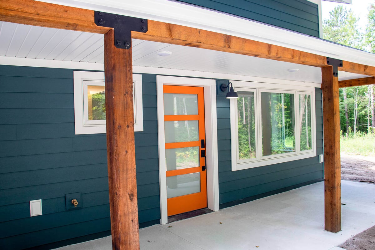 Bright orange front door of a custom-built West Michigan home by R-Value Homes, with contrasting dark siding