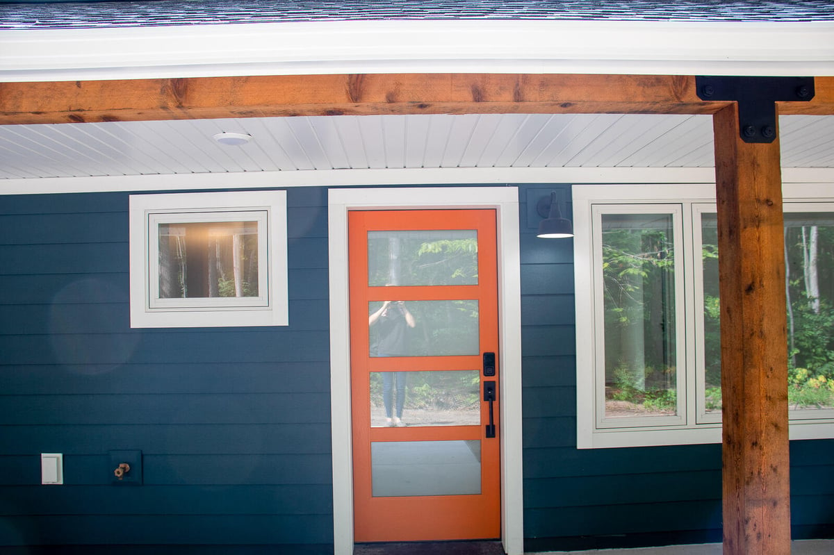 Front porch of a custom home in West Michigan, built by R-Value Homes, featuring an orange door and wooden accents