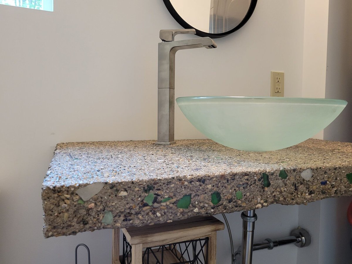 Unique concrete countertop with embedded glass pieces and a glass vessel sink in a custom home by R Value Homes in West Michigan