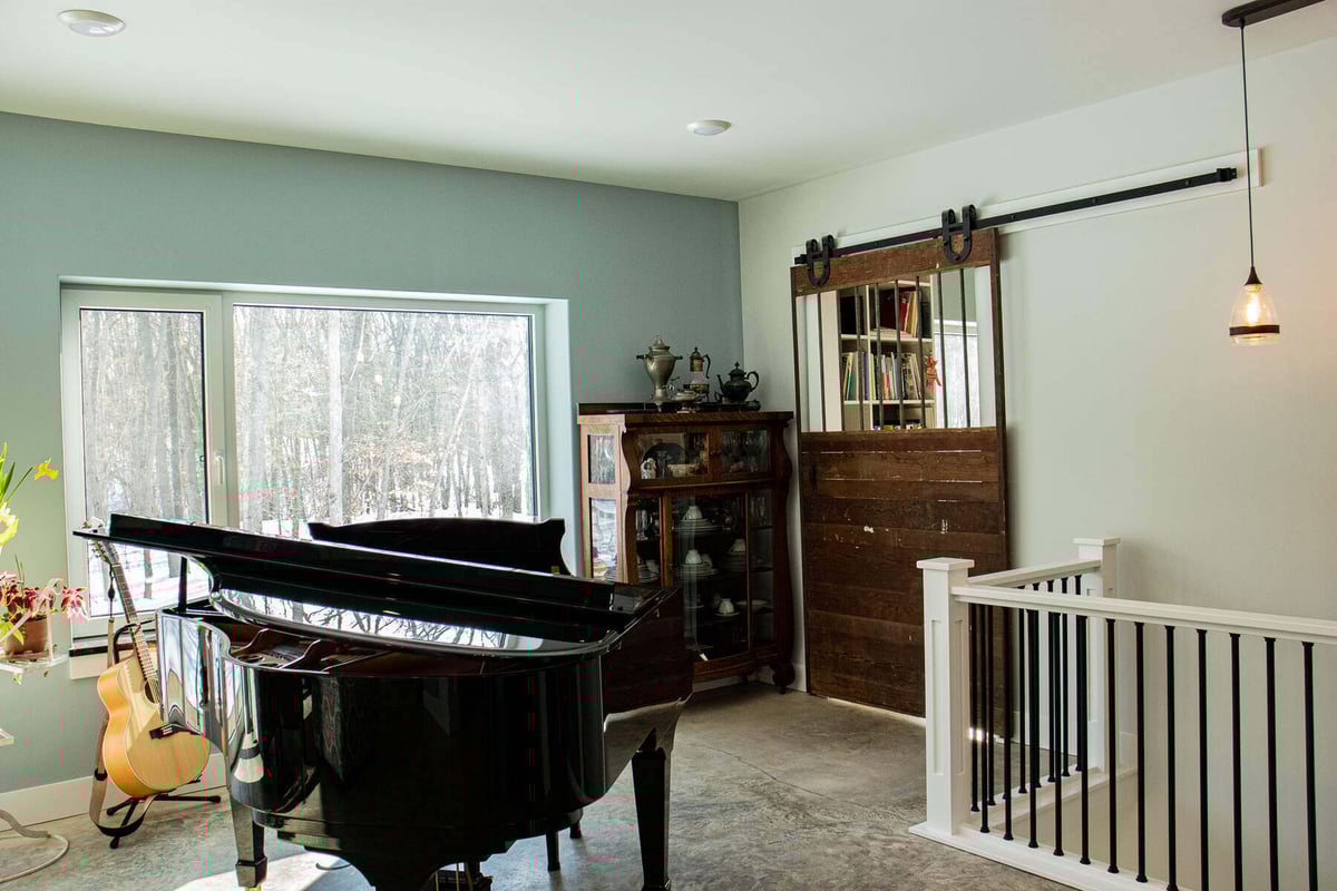Bright room with a grand piano and barn-style decor by R-Value Homes in West Michigan