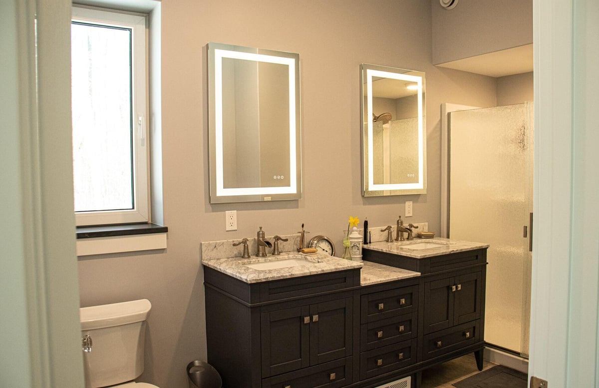 Modern bathroom with double vanities and illuminated mirrors by R-Value Homes in West Michigan