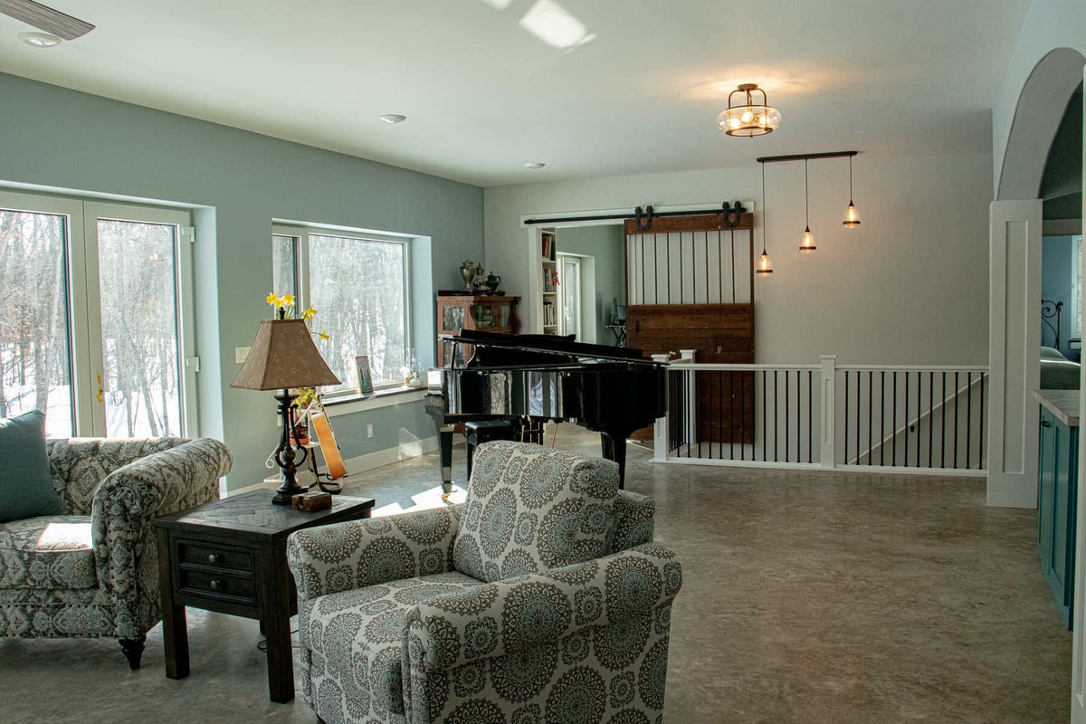 Open-concept living room with a grand piano and large windows by R-Value Homes in West Michigan